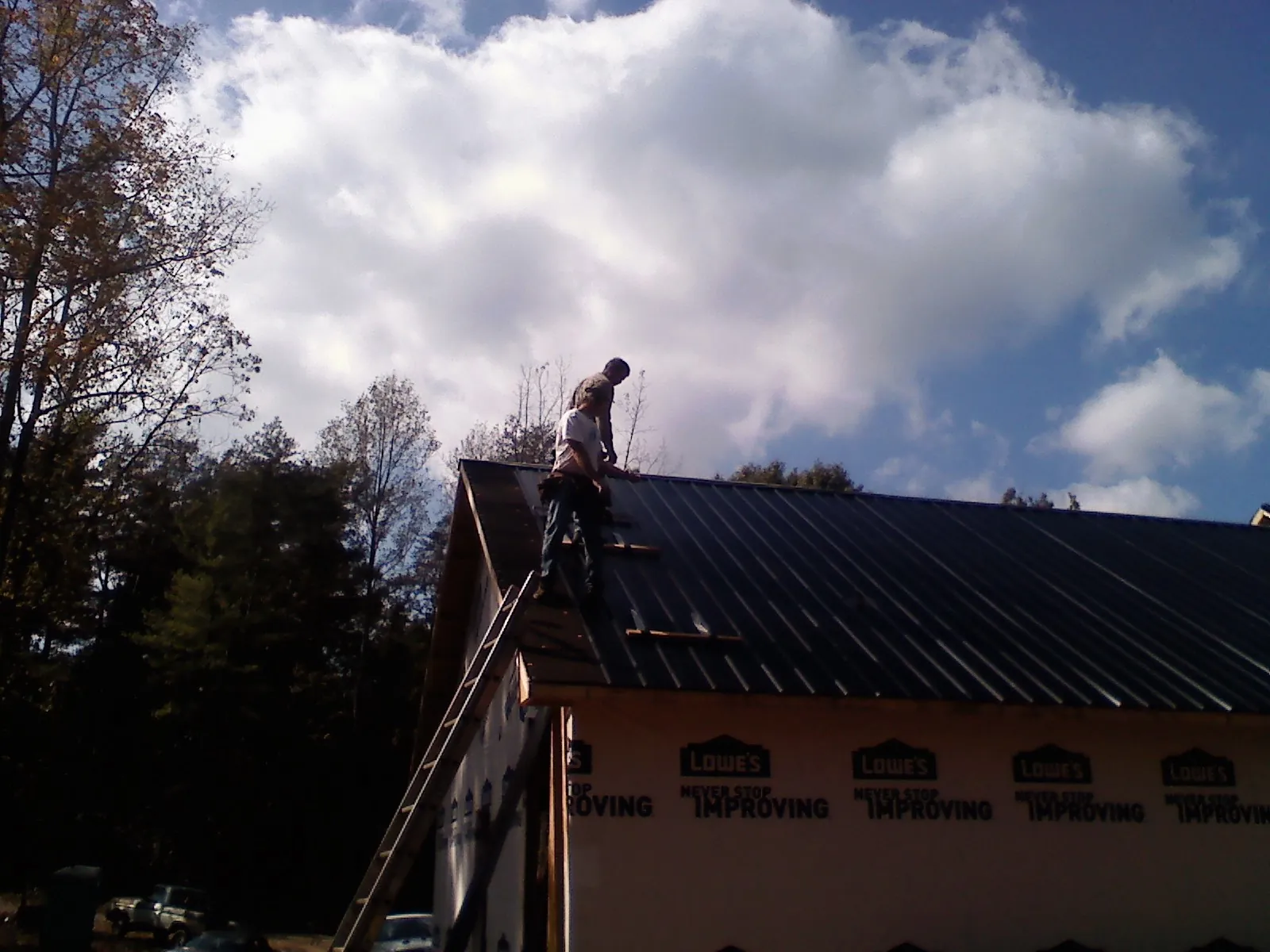 Roofer fastening dark metal panels high against a cloudy sky, from a Roof Inspection job in Berkshire